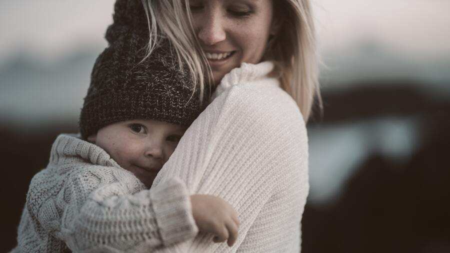 Una mujer con un jersey claro sostiene a un niño pequeño vestido con un gorro de punto y un jersey. El niño mira a la cámara mientras la mujer sonríe mirando hacia abajo, creando un momento cálido captado con el procedimiento sumario en mente. El fondo está suavemente difuminado. Una mujer con un jersey claro sostiene a un niño pequeño vestido con un gorro de punto y un jersey. El niño mira a la cámara mientras la mujer sonríe mirando hacia abajo, creando un momento cálido captado con el procedimiento sumario en mente. El fondo está suavemente difuminado.