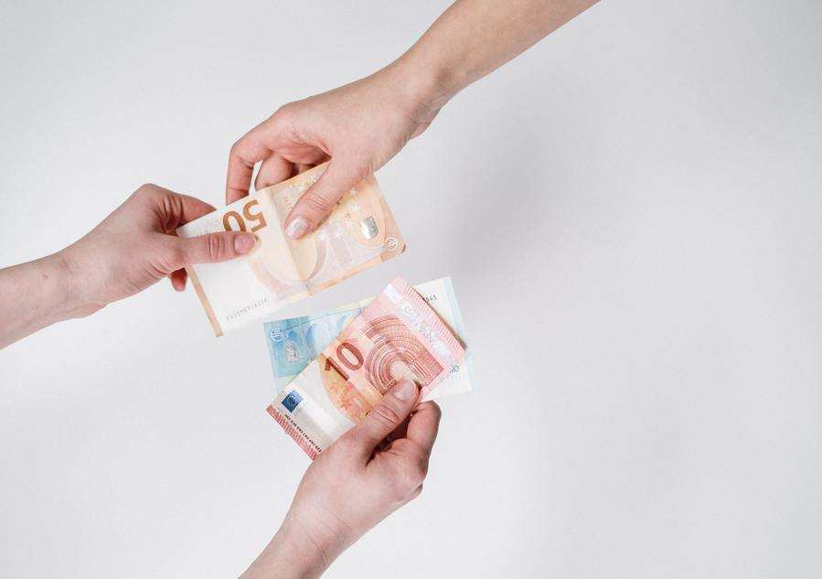Una persona entrega a otra varios billetes de 50, 20 y 10 euros sobre un fondo blanco liso, sugiriendo una prestación compensatoria.