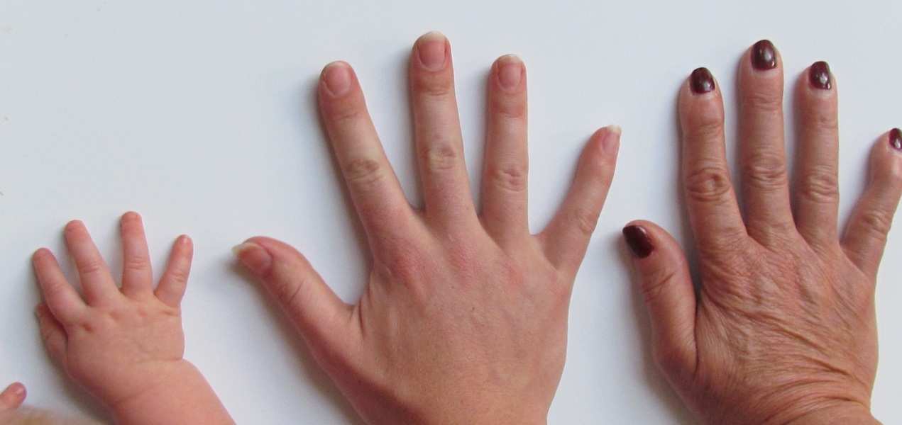 Tres manos de distintas edades descansan una al lado de la otra sobre una superficie blanca: la mano de un bebé a la izquierda, la de un adulto en el centro y la de una persona mayor con las uñas pintadas de oscuro, simbolizando los lazos familiares y la importancia del régimen de visitas abuelos.