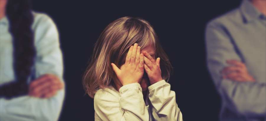 En el centro, una niña se cubre la cara con ambas manos. Dos adultos, posiblemente implicados en un acuerdo de custodia compartida, están a ambos lados de ella sobre un fondo oscuro.