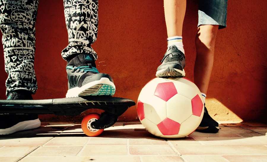 Primer plano de las piernas de tres niños -uno sobre un monopatín, otro haciendo equilibrios sobre un balón de fútbol rojo y blanco y otro con los dos pies apoyados en el suelo- contra una pared naranja y un suelo de baldosas, captando momentos de juventud antes de que surjan gastos extraordinarios. Primer plano de las piernas de tres niños -uno sobre un monopatín, otro haciendo equilibrios sobre un balón de fútbol rojo y blanco y otro con los dos pies apoyados en el suelo- contra una pared naranja y un suelo de baldosas, captando momentos de juventud antes de que surjan gastos extraordinarios.