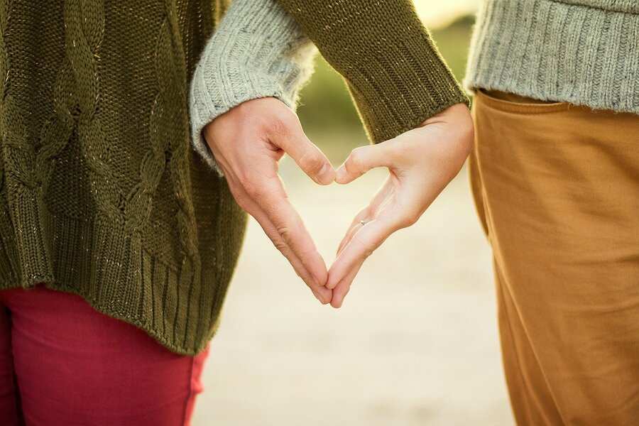 Dos personas muy juntas forman un corazón con sus manos, simbolizando la unidad aunque algunos opten por extinguir la pareja de hecho. Uno lleva un jersey verde y pantalones rojos; el otro, un jersey claro y pantalones marrones. El fondo está desenfocado.