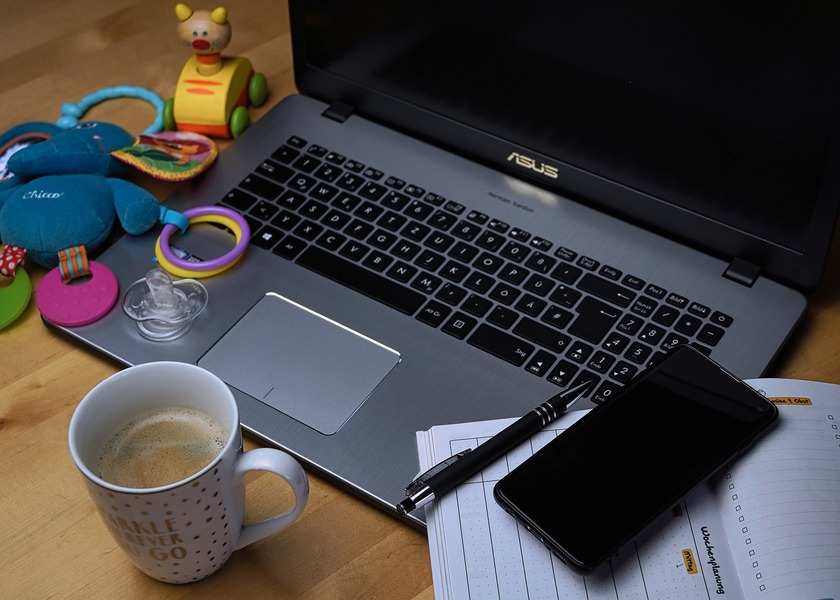 Un portátil sobre un escritorio con un smartphone, un bolígrafo, una taza de café, juguetes para el bebé, un chupete y páginas de la agenda ponen de manifiesto la realidad de la conciliación familiar: una mezcla equilibrada de tareas laborales y elementos esenciales para el cuidado de los niños.