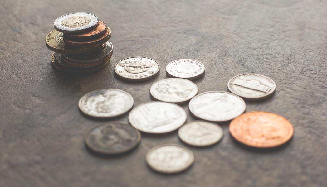 Una pila de monedas diversas está colocada sobre una superficie con textura, y varias monedas más -quizá simbolizando la pensión de alimentos en custodia compartida- están esparcidas cerca de ella en una disposición suelta. Una pila de monedas diversas está colocada sobre una superficie con textura, y varias monedas más -quizá simbolizando la pensión de alimentos en custodia compartida- están esparcidas cerca de ella en una disposición suelta.