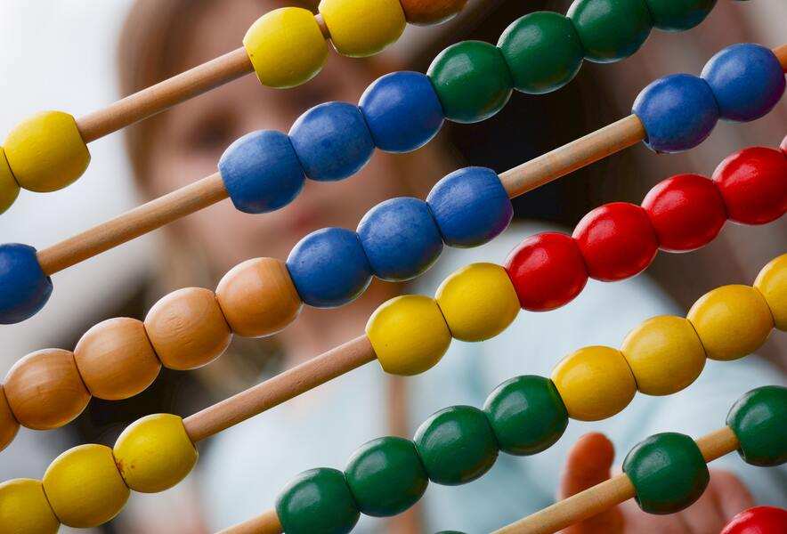 Primer plano de cuentas de colores en un ábaco con un Coordinador Parental borroso al fondo. Las cuentas están dispuestas en filas de color amarillo, azul, verde y rojo. Primer plano de cuentas de colores en un ábaco con un Coordinador Parental borroso al fondo. Las cuentas están dispuestas en filas de color amarillo, azul, verde y rojo.