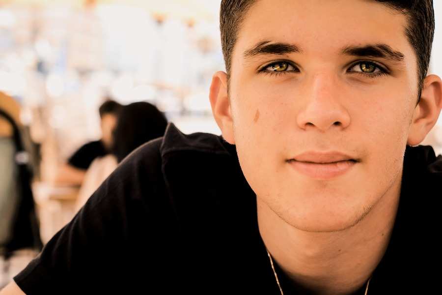 Un joven de pelo corto y oscuro y ojos color avellana mira a la cámara, sonriendo ligeramente. Lleva una camisa oscura y está al aire libre, quizá hablando de temas como la pensión de alimentos a hijos mayores de edad, con otras personas borrosas al fondo. Un joven de pelo corto y oscuro y ojos color avellana mira a la cámara, sonriendo ligeramente. Lleva una camisa oscura y está al aire libre, quizá hablando de temas como la pensión de alimentos a hijos mayores de edad, con otras personas borrosas al fondo.