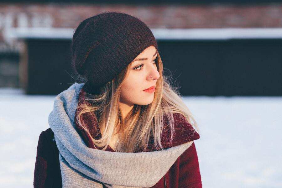 Una mujer joven con abrigo y bufanda en un paisaje nevado.