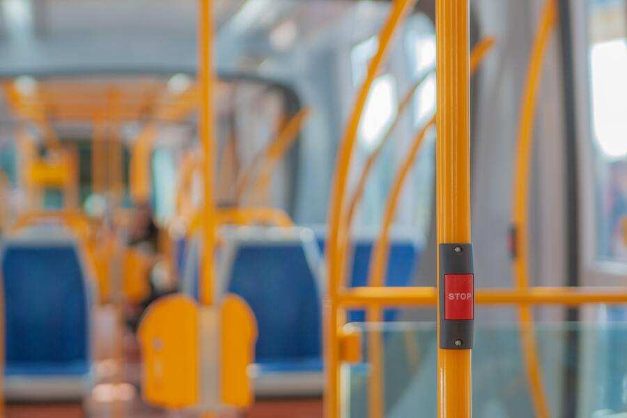 Primer plano de un botón rojo de parada en un poste amarillo dentro de un autobús urbano, con asientos azules y amarillos en el fondo borroso, que ilustra la movilidad geográfica de camino al centro de trabajo. Primer plano de un botón rojo de parada en un poste amarillo dentro de un autobús urbano, con asientos azules y amarillos en el fondo borroso, que ilustra la movilidad geográfica de camino al centro de trabajo.