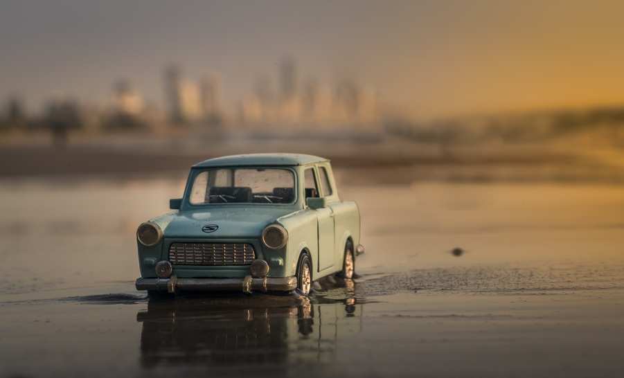Un pequeño coche azul de juguete se posa sobre la arena mojada de la playa con el horizonte borroso de la ciudad de fondo durante la puesta de sol, recordando a un carnet conducir o a un inesperado gasto extraordinario en los viajes de ensueño por carretera. Un pequeño coche azul de juguete se posa sobre la arena mojada de la playa con el horizonte borroso de la ciudad de fondo durante la puesta de sol, recordando a un carnet conducir o a un inesperado gasto extraordinario en los viajes de ensueño por carretera.