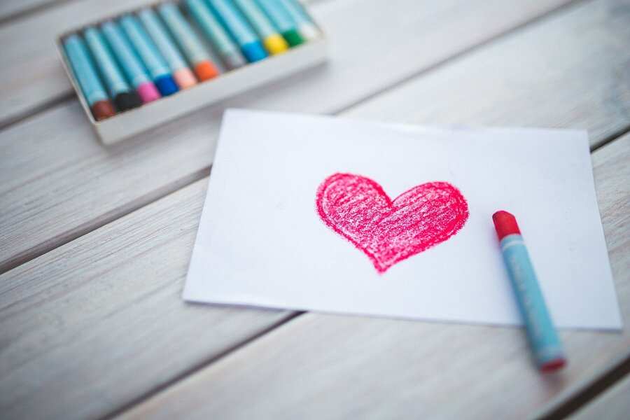 Sobre una superficie de madera, junto a un lápiz de color rojo y una caja abierta de lápices de colores variados, descansa una hoja de papel blanco con un corazón dibujado con lápices rojos, que simboliza el amor, al igual que el proceso de cómo hacerse pareja de hecho.