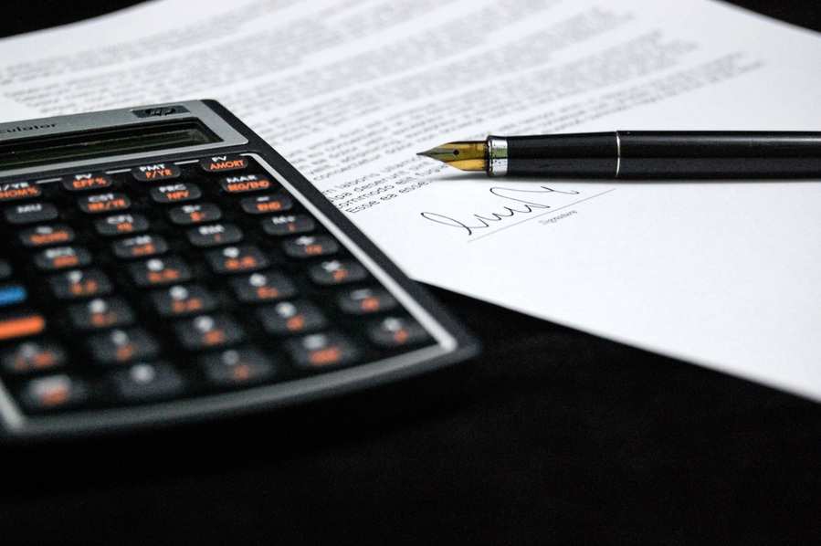 Sobre una superficie oscura se colocan una calculadora negra, una pluma estilográfica negra y dorada y un documento firmado con un texto impreso sobre despedir si estoy en ERTE.