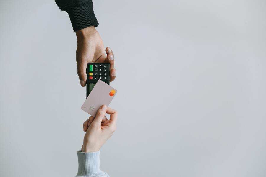 Una persona sostiene un terminal de pago mientras otra se dispone a pagar con una tarjeta de crédito rosa, destacando las transacciones modernas -como la gestión de pensión de alimentos en verano- sobre un fondo claro liso. Una persona sostiene un terminal de pago mientras otra se dispone a pagar con una tarjeta de crédito rosa, destacando las transacciones modernas -como la gestión de pensión de alimentos en verano- sobre un fondo claro liso.