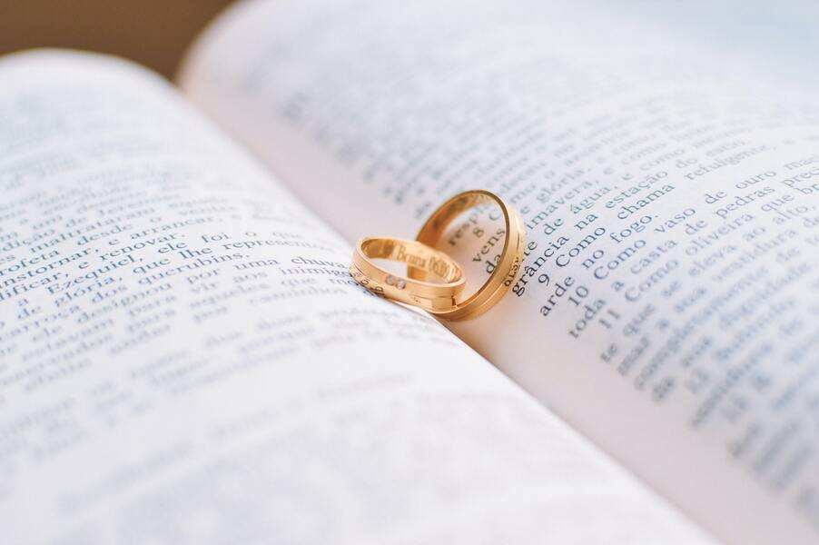 Dos alianzas de oro descansan sobre las páginas abiertas de un libro, y sus sombras forman un corazón en el centro, símbolo de una boda ante notario. El texto de las páginas está en portugués.