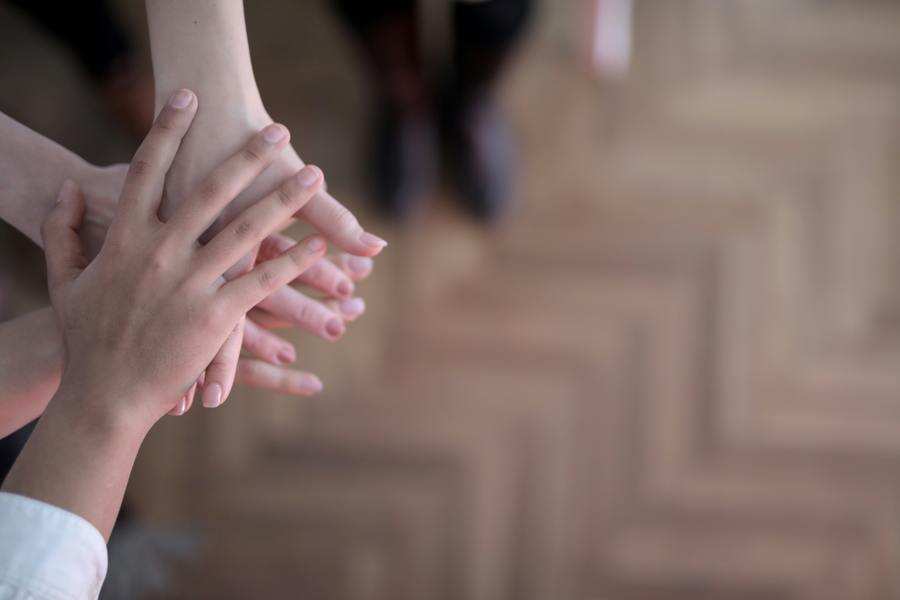 Varias manos se extienden y se apilan unas sobre otras sobre un suelo de madera, sugiriendo trabajo en equipo o unidad, incluso cuando se afrontan retos como la incapacitación familiar. El fondo está difuminado y el foco se centra en las manos.