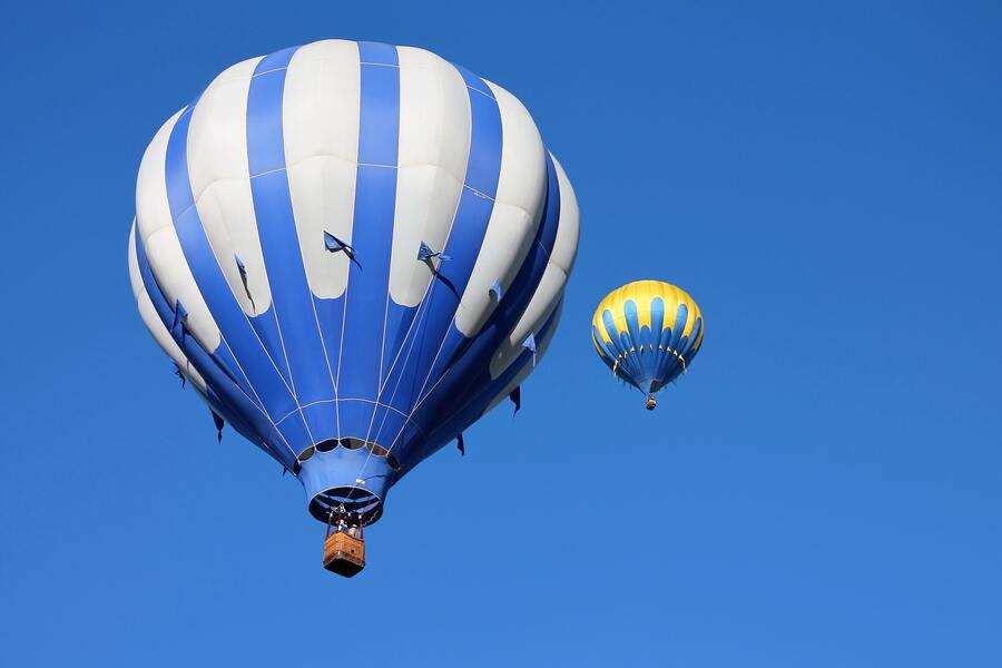 Dos globos aerostáticos flotan en un cielo azul despejado; el globo más grande es azul y blanco con una cesta debajo, y el globo más pequeño flota libremente en la distancia, simbolizando la emancipación del menor de edad. Dos globos aerostáticos flotan en un cielo azul despejado; el globo más grande es azul y blanco con una cesta debajo, y el globo más pequeño flota libremente en la distancia, simbolizando la emancipación del menor de edad.