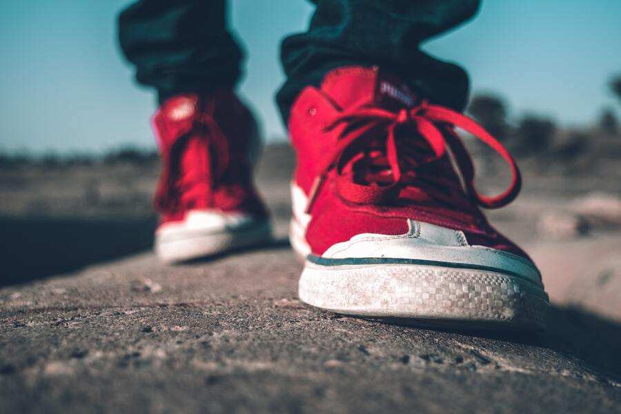 Primer plano de una persona con zapatillas rojas de pie sobre una superficie rugosa al aire libre, simbolizando los primeros pasos hacia la emancipación del menor de edad.