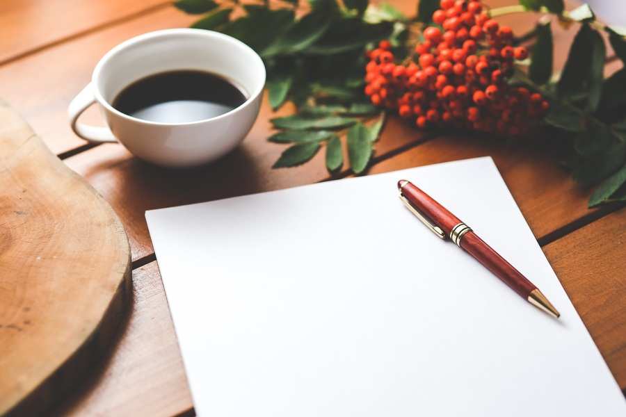 Una hoja de papel blanco y un bolígrafo rojo sobre una mesa de madera, con una taza de café solo y un racimo de bayas rojas con hojas verdes cerca: un escenario ideal para redactar notas sobre el despido disciplinario. Una hoja de papel blanco y un bolígrafo rojo sobre una mesa de madera, con una taza de café solo y un racimo de bayas rojas con hojas verdes cerca: un escenario ideal para redactar notas sobre el despido disciplinario.