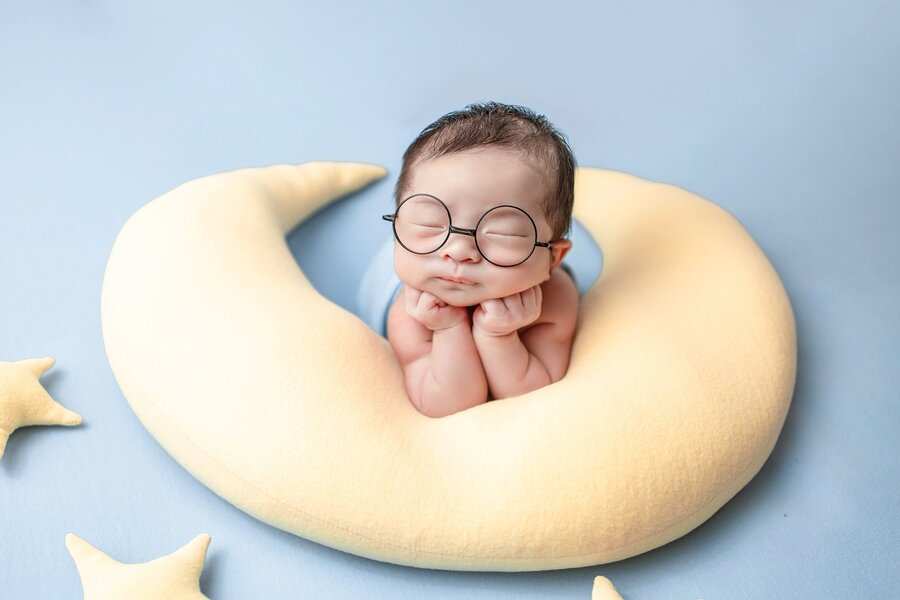Un bebé con gafas redondas descansa sobre una almohada en forma de luna creciente, con las manos bajo la barbilla, rodeado de cojines en forma de estrella: una escena serena que refleja la esperanza de ampliar el permiso de maternidad a las familias monoparentales. Un bebé con gafas redondas descansa sobre una almohada en forma de luna creciente, con las manos bajo la barbilla, rodeado de cojines en forma de estrella: una escena serena que refleja la esperanza de ampliar el permiso de maternidad a las familias monoparentales.