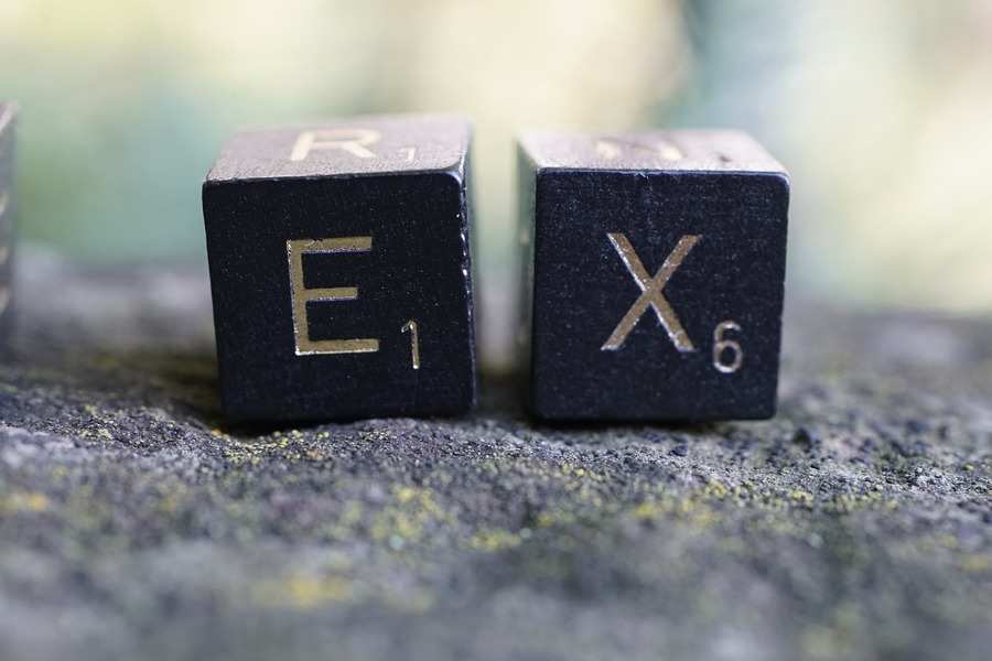 Dos fichas negras de Scrabble con las letras E y X doradas, que representan los valores 1 y 6, se sitúan una al lado de la otra sobre una superficie gris texturizada. El fondo difuminado evoca sutilmente temas como la pensión compensatoria en una composición reflexiva. Dos fichas negras de Scrabble con las letras E y X doradas, que representan los valores 1 y 6, se sitúan una al lado de la otra sobre una superficie gris texturizada. El fondo difuminado evoca sutilmente temas como la pensión compensatoria en una composición reflexiva.