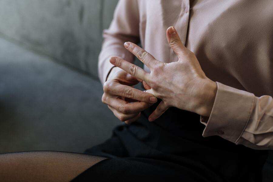 Una persona vestida con blusa rosa claro y falda oscura está sentada y, con la mano derecha, se quita un anillo del dedo anular de la mano izquierda, tal vez preguntándose: ¿puedo negarme a firmar el divorcio? No se ve su rostro.