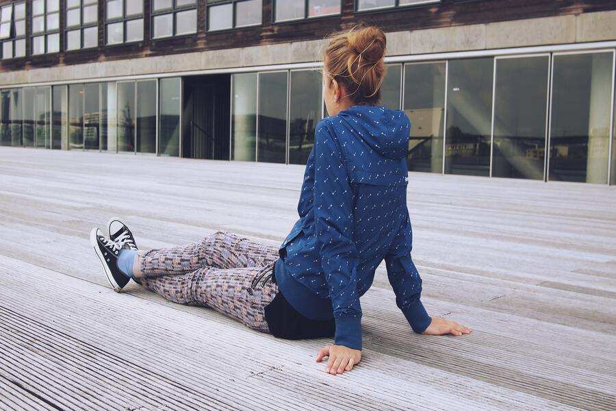 Una persona con sudadera azul con capucha, pantalones estampados y zapatillas negras se sienta en una terraza de madera, aparentemente ensimismada en sus pensamientos sobre mi hijo no quiere saber de mi y pensión de alimentos, con un moderno edificio de grandes ventanales a sus espaldas. Una persona con sudadera azul con capucha, pantalones estampados y zapatillas negras se sienta en una terraza de madera, aparentemente ensimismada en sus pensamientos sobre mi hijo no quiere saber de mi y pensión de alimentos, con un moderno edificio de grandes ventanales a sus espaldas.
