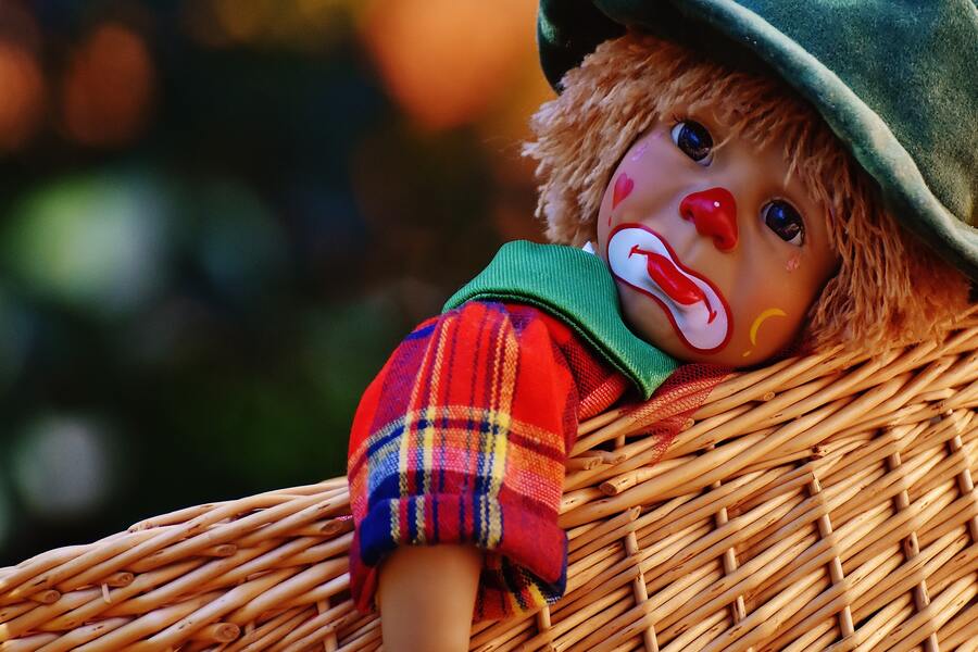 Un muñeco vestido de payaso triste, con los rasgos faciales pintados, la nariz roja y ropas de colores, descansa sobre una superficie de mimbre tejido, encarnando la tristeza de un caso de delito impago de alimentos. El muñeco lleva un sombrero y un pañuelo verdes.