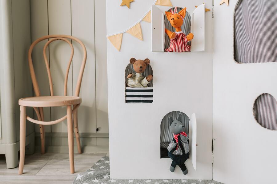 Una casita blanca con ventanas recortadas muestra un zorro de peluche, un osito de peluche y un muñeco de gato gris, perfectos para aventuras imaginativas sobre patria potestad y custodia. A la izquierda hay una silla de madera, con una alfombra gris estampada y un alegre banderín amarillo en la pared. Una casita blanca con ventanas recortadas muestra un zorro de peluche, un osito de peluche y un muñeco de gato gris, perfectos para aventuras imaginativas sobre patria potestad y custodia. A la izquierda hay una silla de madera, con una alfombra gris estampada y un alegre banderín amarillo en la pared.