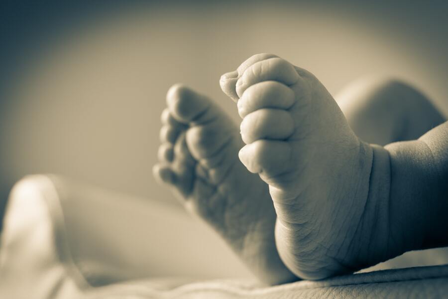 Primer plano de los pies de un bebé con los dedos visibles, descansando sobre una superficie blanda. La foto en blanco y negro, suavemente enfocada con un fondo difuminado, evoca sutilmente temas de filiación y tiernos comienzos.