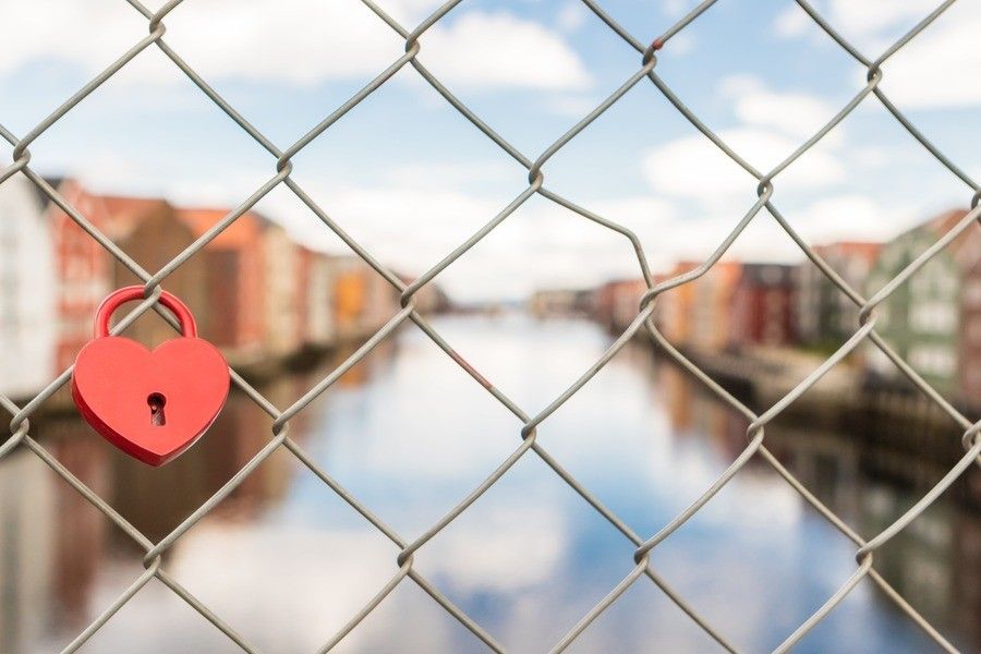 Un candado rojo en forma de corazón, símbolo de los bienes privativos, está sujeto a una alambrada que da a un canal borroso y a edificios lejanos.