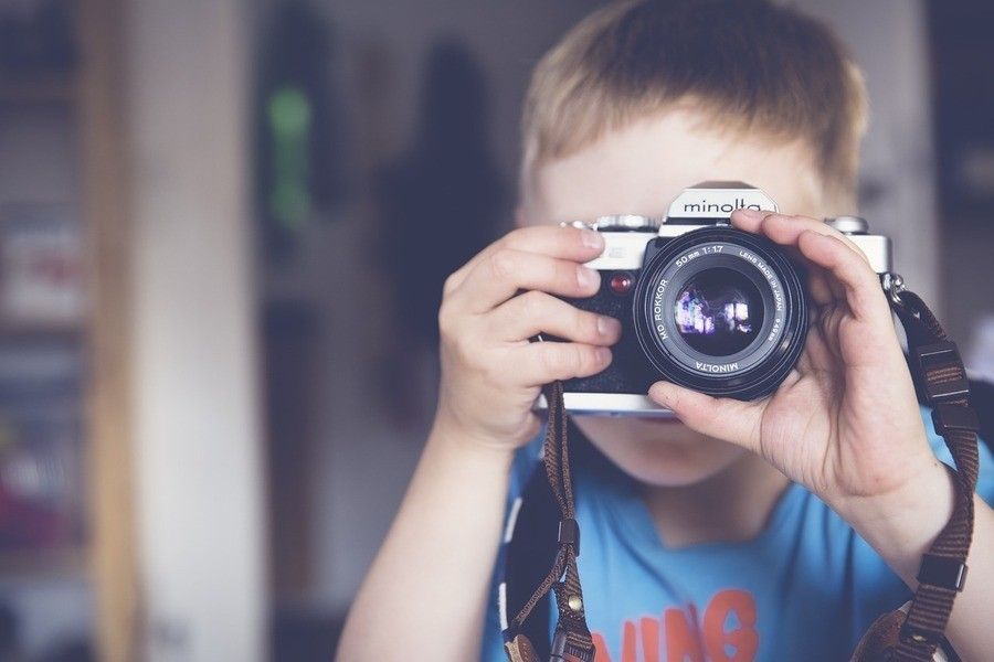 Un niño de corta edad se acerca a la cara una cámara Minolta para hacer una fotografía. El niño lleva una camisa azul, con un fondo suavemente difuminado, lo que subraya la importancia de no publicar imágenes de menores sin consentimiento. Un niño de corta edad se acerca a la cara una cámara Minolta para hacer una fotografía. El niño lleva una camisa azul, con un fondo suavemente difuminado, lo que subraya la importancia de no publicar imágenes de menores sin consentimiento.