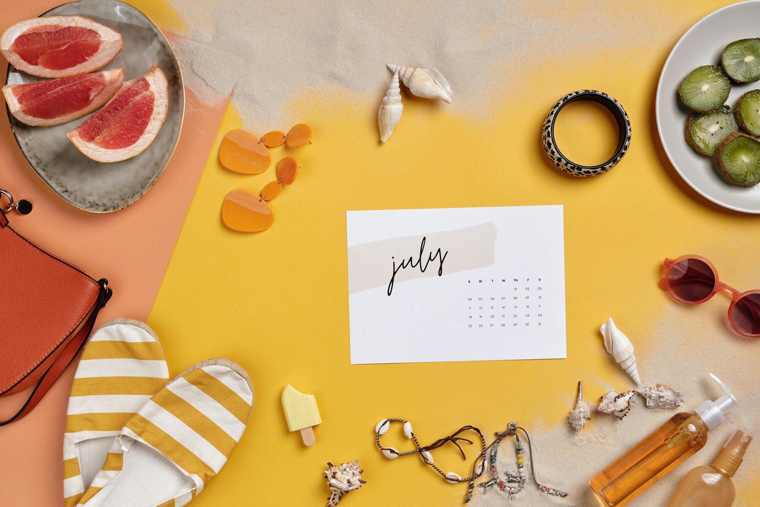 Una composición plana de artículos veraniegos sobre arena y amarillo, incluido un calendario de julio -perfecto para planificar el reparto de vacaciones veraniegas-, además de gafas de sol, sandalias, pomelos, kiwis, joyas, conchas marinas, un bolso, pendientes, crema solar, pulsera y un artículo con forma de helado. Una composición plana de artículos veraniegos sobre arena y amarillo, incluido un calendario de julio -perfecto para planificar el reparto de vacaciones veraniegas-, además de gafas de sol, sandalias, pomelos, kiwis, joyas, conchas marinas, un bolso, pendientes, crema solar, pulsera y un artículo con forma de helado.