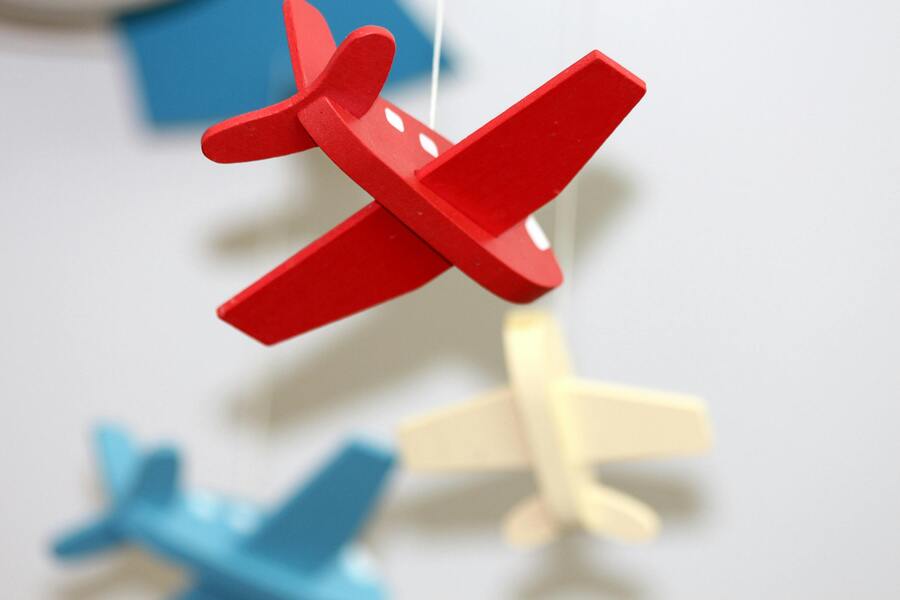 Informes psicosociales en custodia compartida Primer plano de un avión de juguete de madera roja colgado de una cuerda, con aviones de madera azul y crema difuminados en el fondo contra una pared lisa de color claro.